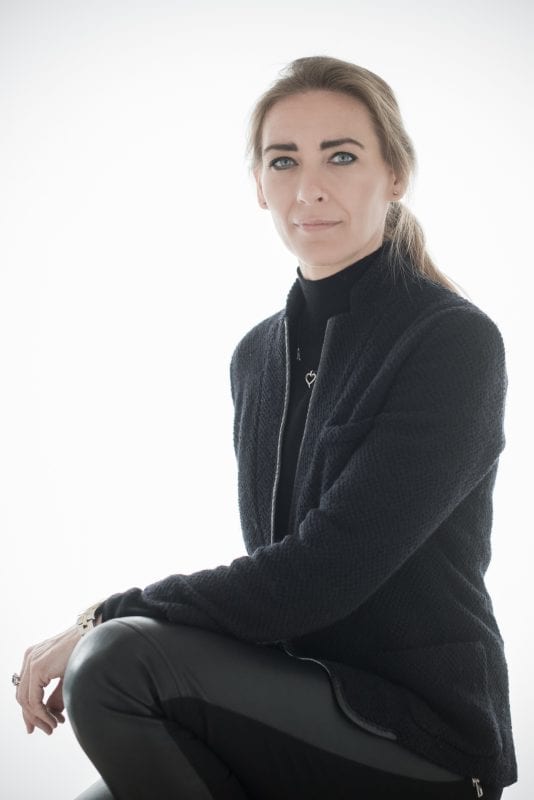 En kvinde med langt lysebrunt hår bundet tilbage sidder klædt i en sort struktureret jakke, sort rullekrave og sorte læderbukser mod en hvid baggrund - og indfanger den selvsikre tilstedeværelse af en privat socialrådgiver. Hun kigger neutralt ind i kameraet.